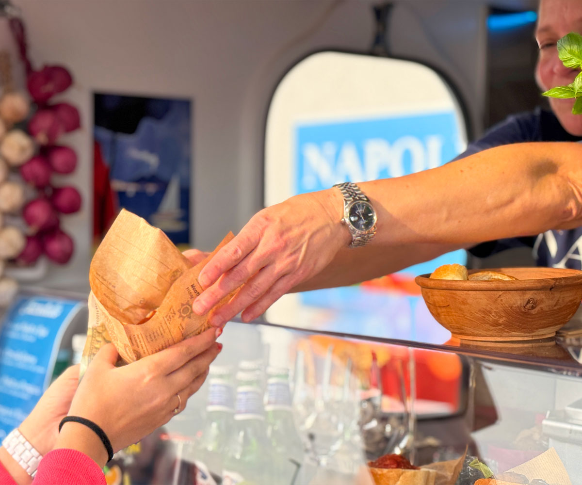 Eine Frau reicht über den Tresen eines Foodtrucks etwas in Papier gewickeltes aus einem Foodtruck.